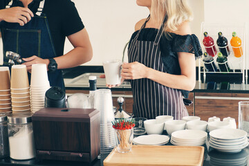 Male and female barista busy preparing coffee and tea menu behind the bar at their cafe. Coffee...