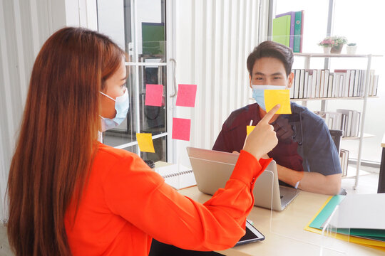 Young Asian colleagues wearing face masks working at the office with screen separated each other to prevent the Covid 19 virus for good health and hygiene at workplace and social distancing concept