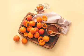 Board with tasty ripe apricots and jam on color background