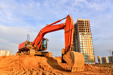 Excavator during excavation at construction site on sunset background. Red Backhoe on road work....