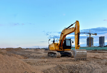 Excavator during road work at construction site. Screeding the gravel for laying asphalt and installing borders and curbs on the new road. Tower crane in action