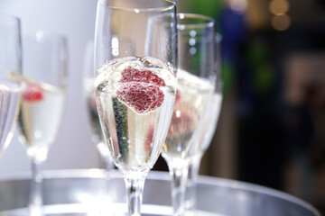 Serving tray with glasses of champagne with raspberry in close up at the event.