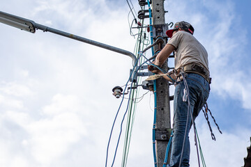 Electricians working on power pole connecting cables with clear sky background.- Concept of...