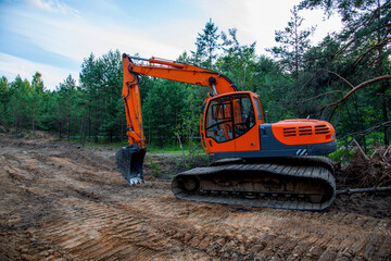 Excavator clearing forest for new development. Orange Backhoe modified for forestry work. Tracked heavy power machinery for forest and peat industry. Logging, road construction in forests. Soft Focus