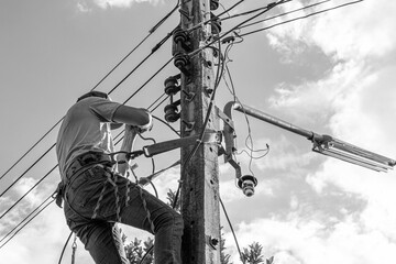 Electricians working on power pole connecting cables with clear sky background.- Concept of...