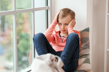 Sad little boy with autistic disorder sitting near window at home