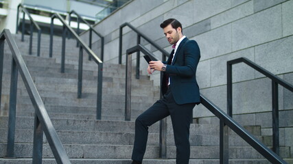 Businessman laughing with phone in hand at street. Man using smartphone outdoor