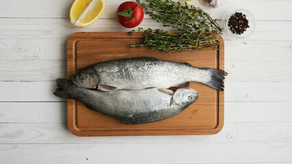 Two rainbow trout on a board, with herbs , ready for cooking.