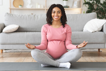 Happy black expecting lady meditating at home