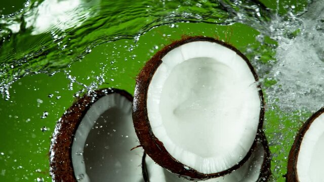 Super Slow Motion Shot of Flying Fresh Coconuts and Water Side Splash on Green Background at 1000fps.