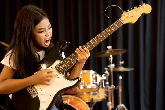 A cute young Asian elementary school girl with long hair playing with serious electric guitar in rock songs.