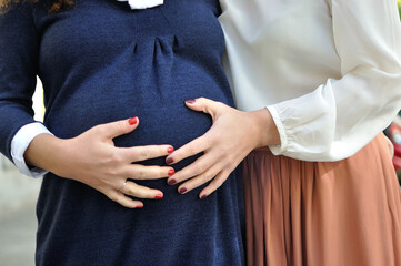Two LGBT mothers are waiting for their baby, a detailed picture of the pregnancy with their hands.