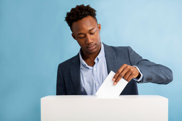 African american man putting ballot in election box over blue