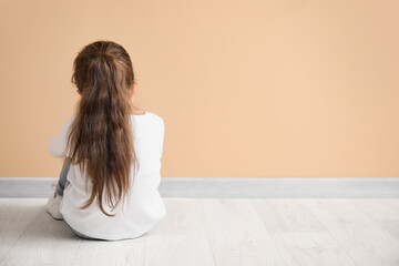 Sad little girl with autistic disorder sitting near color wall, back view
