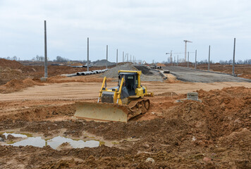 Bulldozer moves gravel during on road work at construction site. Dozer leveling stones for laying asphalt on a new freeway. Heavy machinery for earth-moving
