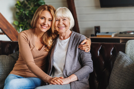 Portrait of elderly mother and middle aged daughter smiling together on the couch at home