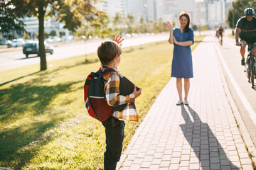A mother walks her son to school. Mom Waves goodbye to the boy, and he waves back. The concept of training and education, a place for text