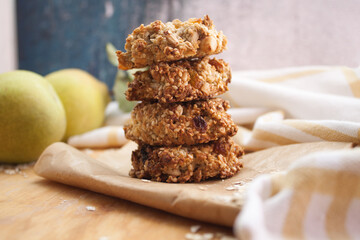 Homemade oatmeal cookies folded in a pile on baking paper with pears behind. Wooden background
