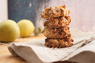Homemade oatmeal cookies folded in a pile on baking paper with pears and wooden spoon behind. Wooden background
