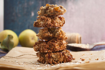 Homemade oatmeal cookies folded in a pile on baking paper with pears and wooden spoon behind. Violet grunge background
