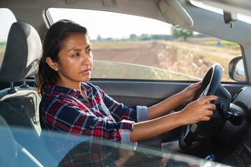 Positive hispanic woman driver sitting in car, side view