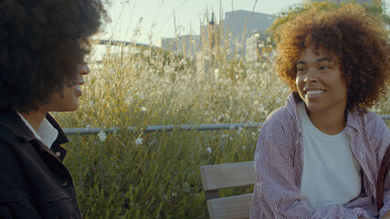 A couple of mixed race black women talking in the park surrounded by flowers in morning sunlight Film colors soft focus