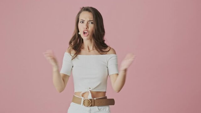 A confused puzzled young woman is refusing of something standing isolated over pink background in studio