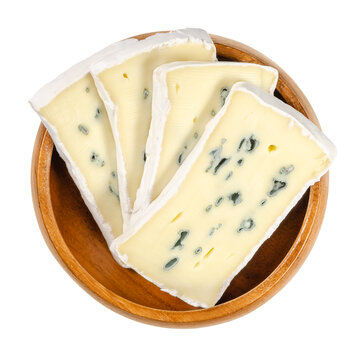Slices of soft cheese with white and blue mold in wooden bowl. Creamy cheese made of cow milk, surface ripened with white fungus and inside of the cheese a blue fungus. Closeup from above, food photo.