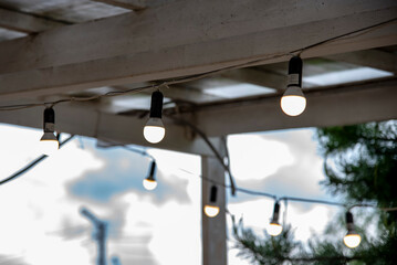 A garland of burning light bulbs hangs under the wooden ceiling of the summer porch.