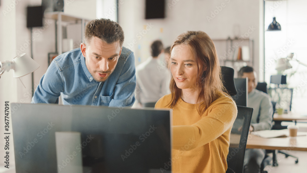 Poster female specialist works on desktop computer, project manager stands beside and gives advice on optim