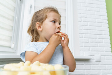 cute little girl puts lots of corn sticks in her mouth and looks at the sides. the concept of greed