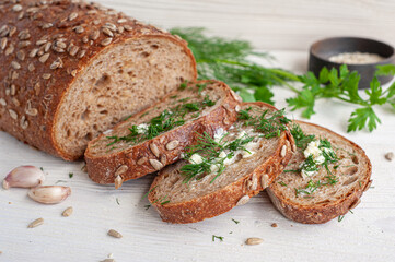 Pieces of whole grain bread with butter, dill, salt and garlic on a white wooden background.