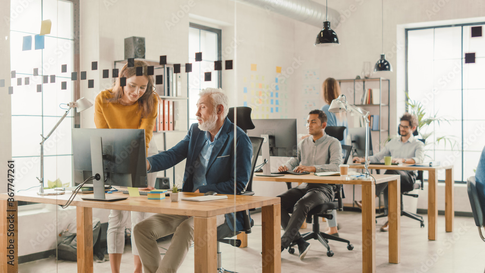 Aufkleber Handsome Middle Aged Creative Engineer Sitting at the Desk working on Desktop Computer Has Discussion with Beautiful Female Project Manager. Office with Friendly Colleagues Chatting, Finding Solutions