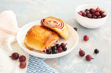 Fresh buns with berry filling decorated with black currants and gooseberry on a light blue concrete background.