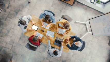 Startup Meeting Room: Team of Entrepreneurs sitting at Conference Table Have Discussions, Solve Problems, Use Digital Tablet, Laptop, Share Documents with Statistics, Charts. Top View Shot © Gorodenkoff