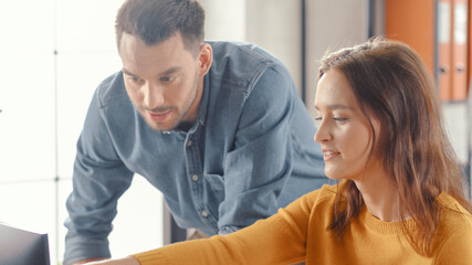 Obraz premium Portrait of Beautiful Female Office Employee Working on Computer, Handsome Project Manager Stands Beside and gives Advice on Optimizing Workflow for Customer Experience Management