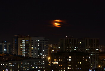 Obraz premium Full moon in the clouds in the city. High-rise buildings from above in the foreground