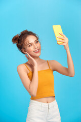 Smiling young woman girl posing isolated on blue background. Doing selfie shot on mobile phone