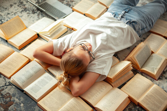 Cute teen girl student in casual clothing and glasses lying on books after holidays, back to school, exam preparation