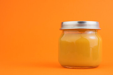 Canned vegetable or fruit puree in a glass jar on an orange background. The concept of baby food, canned food, orange vegetables or fruits. Copy space