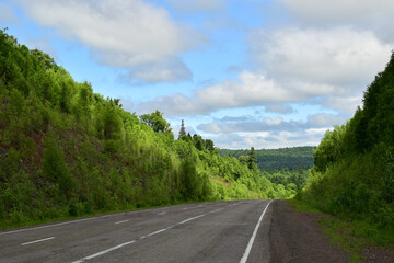 Paved road among green hills. Blue sky with white clouds. Bright summer day.