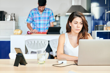 Woman working on her laptop while her husband prepares food according to an internet recipe