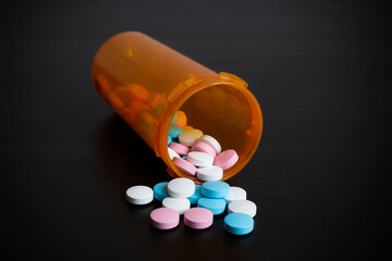 Orange prescription bottle with scattered out colored pills on dark surface