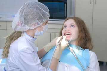 Orthodontist covering special gel on woman teeth and drying it in dentistry before braces installing. Treatment and cure in dentistry. Portrait of girl with retractor in mouth. Correcting teeth.