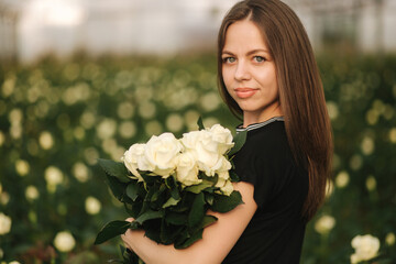 Portrait of beautiful young woman in greenhouse with bouquet of white roses