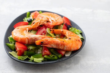 salad with fried shrimps on dark plate on ceramic background