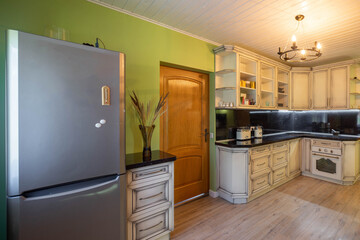 Modern interior of kitchen in private country house. White kitchen set. Green wall. Wooden door. Fridge.