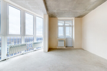 An unfinished room without decoration and with the white plastered walls and the panoramic balcony in a new residential building