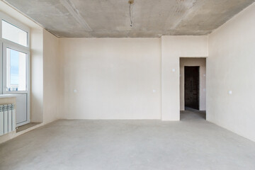 The front view an unfinished residential apartment with the white plastered walls, the empty doorway and the plastic balcony door