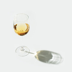 One glass of white wine on light background with hard shadow